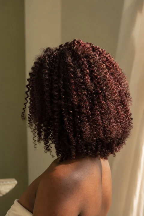 Coily cherry cola hair showing a red flash in warm light against deep brown skin