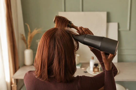 Woman round-brushing curtain bangs back from the center part with a hairdryer